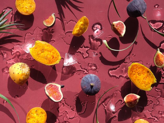 Fruits exotiques poires de barbarie jaunes et oranges fruits de cactus sains sur fond rouge avec des feuilles Télévision directe du soleil avec des ombres Fond humide avec de la glace