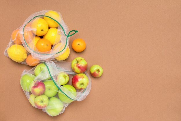 Fruits frais et juteux citrons pommes et mandarines dans des sacs en filet écologiques réutilisables.