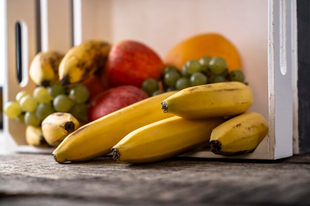 Photo des fruits frais mélangés, des oranges, des pommes, des bananes et des raisins dans une caisse en bois sur des planches en bois rustiques texturées