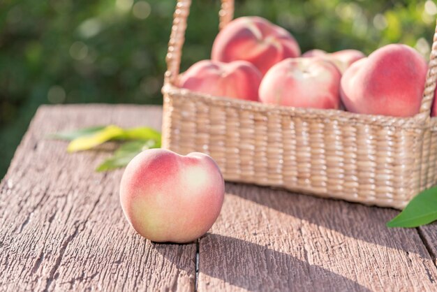 Fruits frais de pêche en arrière-plan flou Pêche dans un panier en bambou sur une table en bois dans le jardin