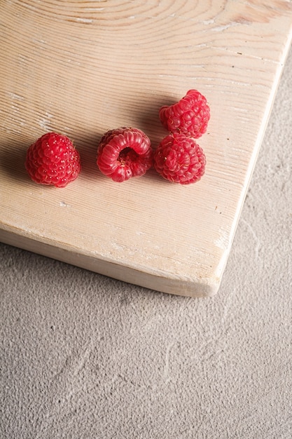 Fruits de framboise sur une vieille planche à découper en bois, tas sain de baies d'été sur la surface de béton en pierre, vue d'angle