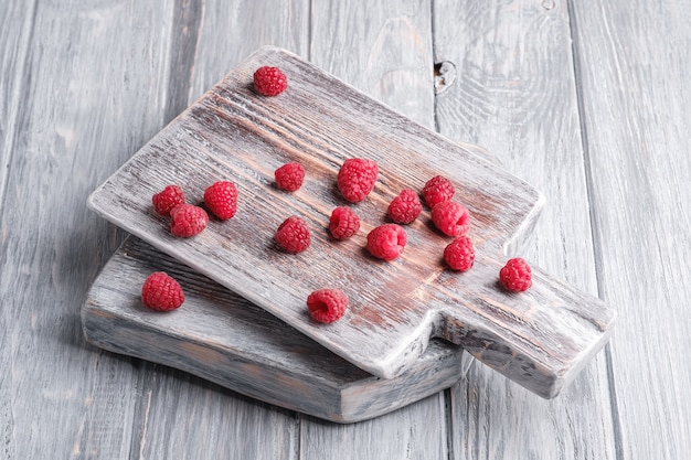 Fruits de framboise sur une vieille planche à découper, tas sain de baies d'été sur une surface en bois gris, vue d'angle