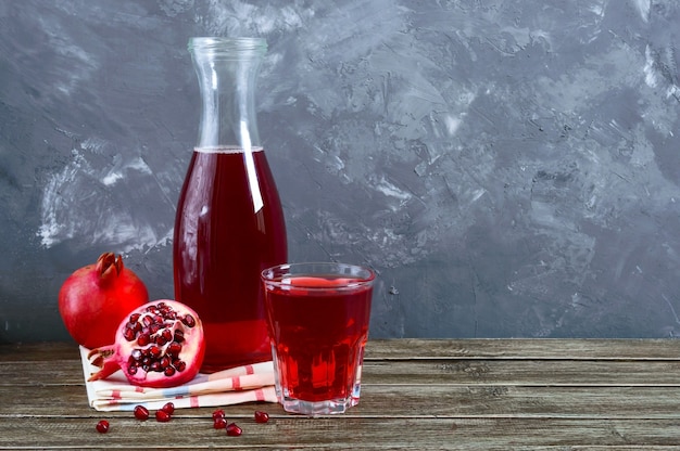 Photo fruits de grenade mûrs, bouteille et verre de jus de grenade frais sur table en bois