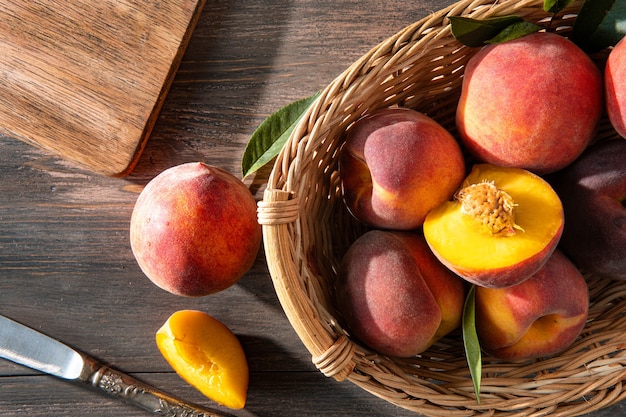 Fruits juteux mûrs sucrés, pêches aux feuilles vertes dans un panier sur un fond en bois foncé sur une planche à découper