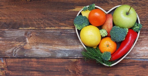 Fruits et légumes dans une boîte en bois en forme de coeur. Brocoli, pommes, poivre, mandarine sur une table en bois. Aliments santé Concept avec fond.