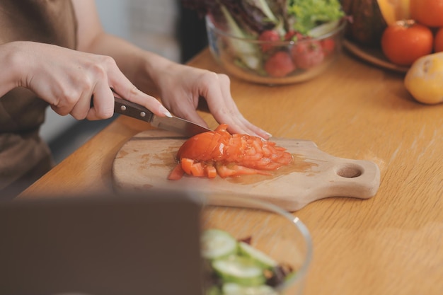 Des fruits et légumes délicieux sur une table et une femme qui cuisine Une femme de maison coupe des concombres verts sur une planche de bois pour faire de la salade fraîche dans la cuisine