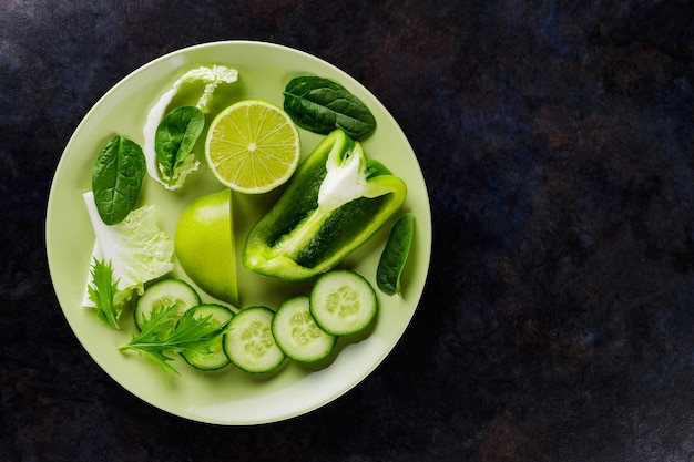 Fruits et légumes verts biologiques sur fond sombre. Aliments diététiques verts sur une assiette. Nourriture saine. Vue de dessus. Espace de copie