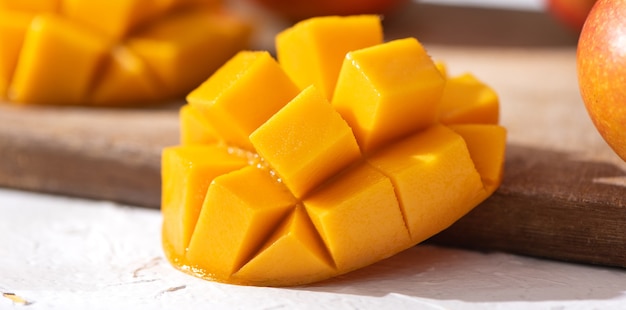 Fruits de mangue fraîche en dés sur une planche à découper en bois avec la lumière du soleil et l'ombre des feuilles dans la cuisine à domicile l'après-midi