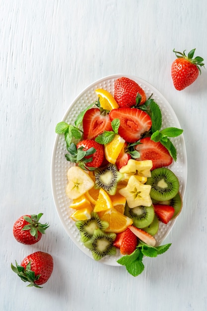 Fruits mûrs colorés et baies sur plateau, vue de dessus sur fond blanc. Concept de cuisine végétarienne. Fraise, kiwi, pomme et orange.