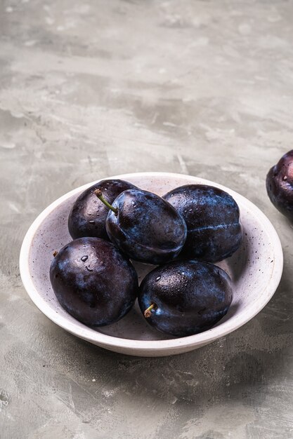 Fruits mûrs frais de prune avec des gouttes d'eau dans un bol en bois sur pierre