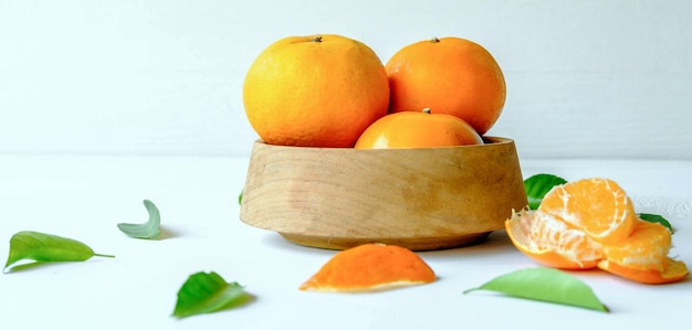 Fruits orange frais dans un bol en bois et feuille d'orange verte sur fond blanc