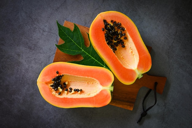 Fruits de papaye sur fond sombre tranche de papaye mûre fraîche coupée en deux fruits tropicaux avec des graines de papaye et des feuilles de papaye vue de dessus