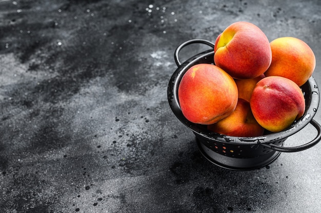 Fruits de pêches dans une passoire noire sur la table.