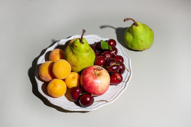 Fruits sur plaque en céramique blanche avec ombre dure sur fond gris mise au point sélective