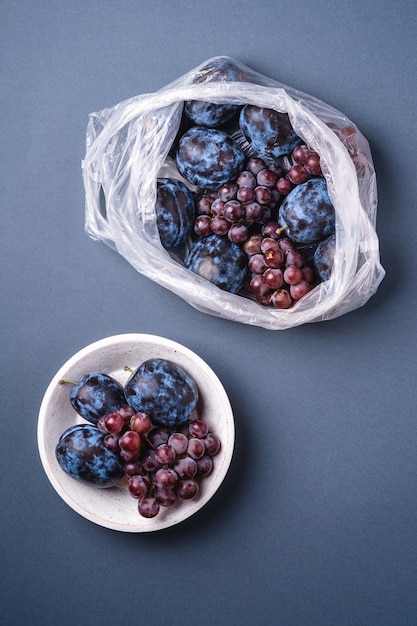 Fruits de prune mûrs frais et baies de raisin dans un sac en plastique et dans un bol en bois