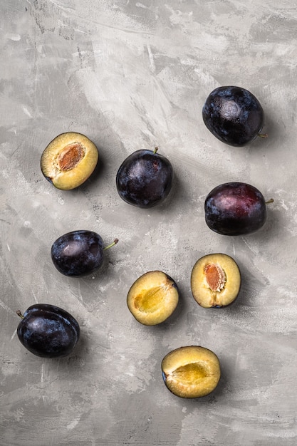 Fruits de prune mûrs frais entiers et tranchés avec des gouttes d'eau sur fond de béton en pierre, vue du dessus