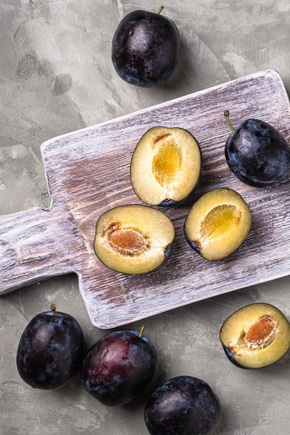 Fruits de prune mûrs frais entiers et tranchés sur une planche à découper en bois, table en béton en pierre, vue de dessus