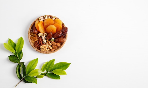 Fruits Secs Et Noix Mélangés Dans Une Assiette En Osier, Branche Avec De Jeunes Feuilles Vertes. Concept De La Fête Juive Tu Bishvat Sur Fond Blanc Avec Copie Espace