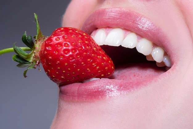 Fruits sexy d'été Gros plan de sourire avec des dents blanches saines Fraise dans les lèvres Fraise rouge dans la bouche de la femme se bouchent