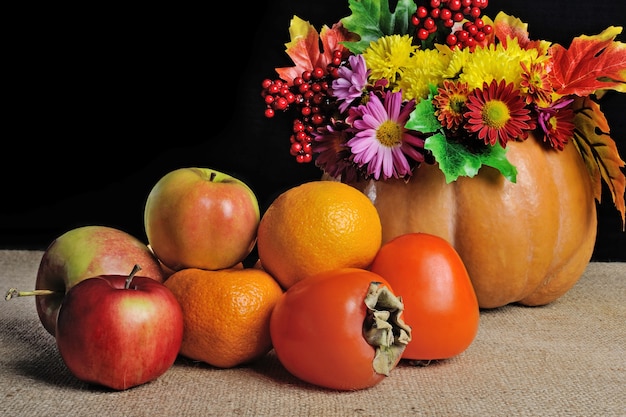 Fruits sur la table avec des fleurs dans un vase citrouille