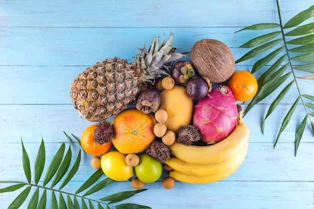 Fruits tropicaux juteux mûrs et feuilles de palmier sur une surface en bois bleue