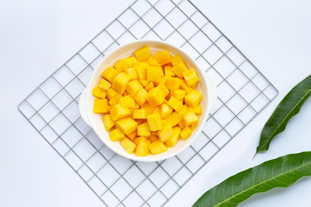 Fruits tropicaux, tranches de cube de mangue dans un bol blanc sur fond blanc.