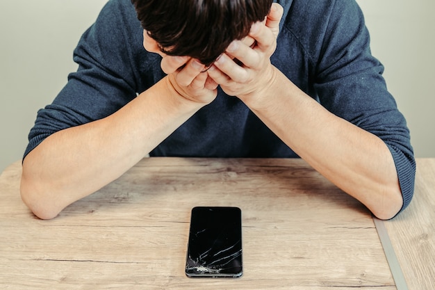 Frustré jeune homme regardant son smartphone cassé