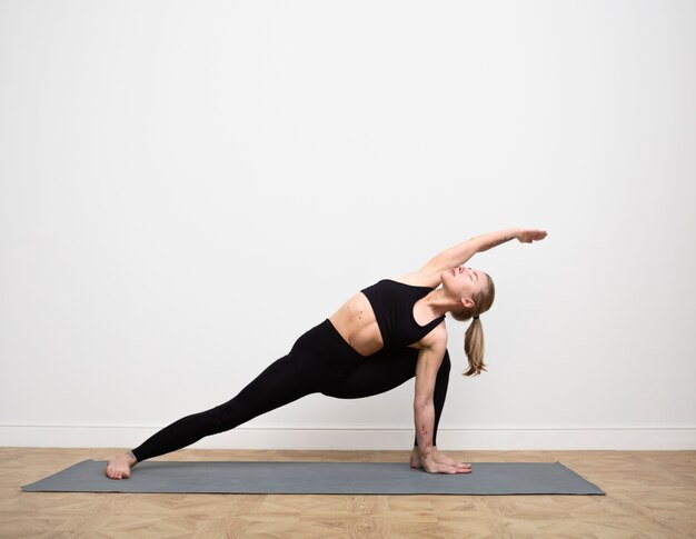 Full shot woman stretching sur tapis de yoga