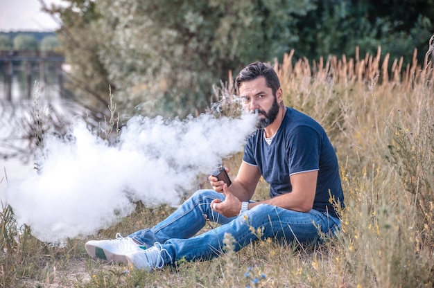 Fumeur brutal élégant exhalant la vapeur de la cigarette électronique à l'air frais