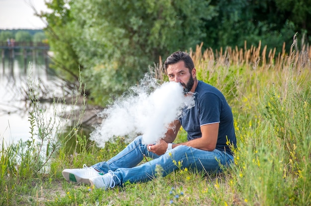 Fumeur brutal élégant fumant une cigarette électronique à la lumière du jour