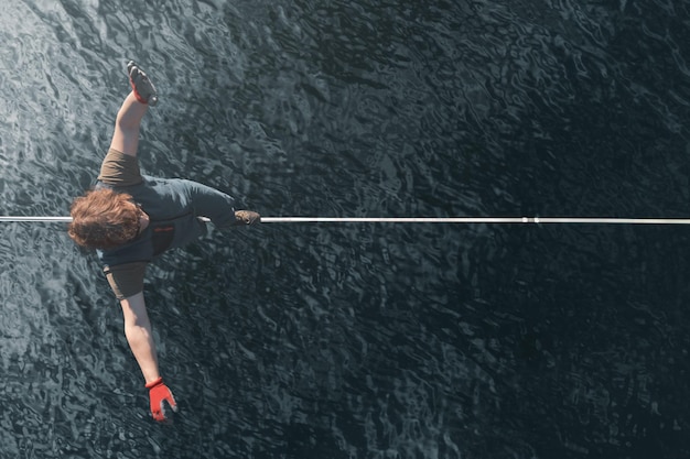 Photo un funambule masculin marche sur une slackline tendue sur la surface miroir de l'eau vue de drone