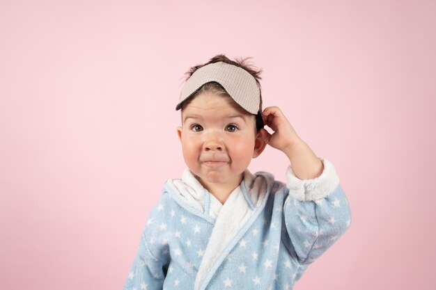 Funny baby boy en peignoir portant un masque de sommeil sur fond rose Time to sleep concept Photo de haute qualité