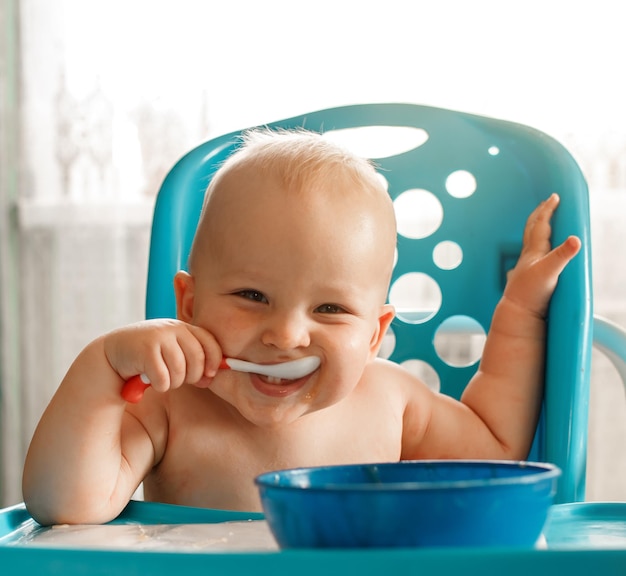 Funny baby kid souriant assis sur une chaise en train de manger de la purée de fruits