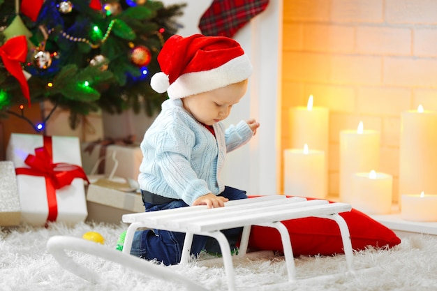 Funny baby sitting près d'un traîneau et d'un arbre de Noël et d'une cheminée sur fond