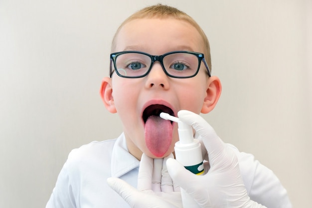 Funny boy avec mal de gorge portant des lunettes, le médecin utilise un aérosol de médecine pour la gorge