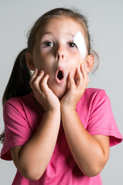 Funny cute adorable petite fille aux cheveux noirs avec une blessure et un patch sur le visage porter une chemise rose Peur de la réaction des parents