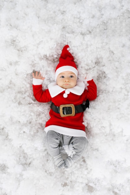 Funny funny baby in Santa costume se trouve dans la neige artificielle.