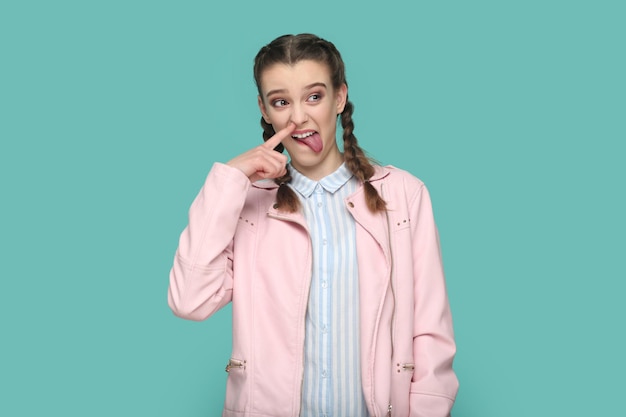 Funny girl adolescente enfantine avec des tresses debout avec le doigt dans le nez qui sort la langue
