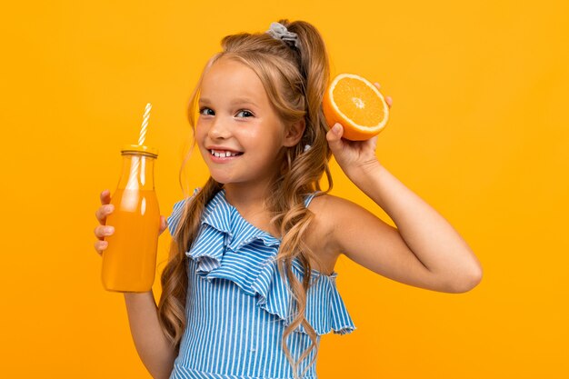 Funny Girl tenant une orange en tranches et une bouteille de jus dans ses mains sur un mur jaune