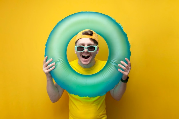 Funny guy touriste dans des vêtements d'été et des lunettes tient un anneau de bain et regarde dedans et sourit