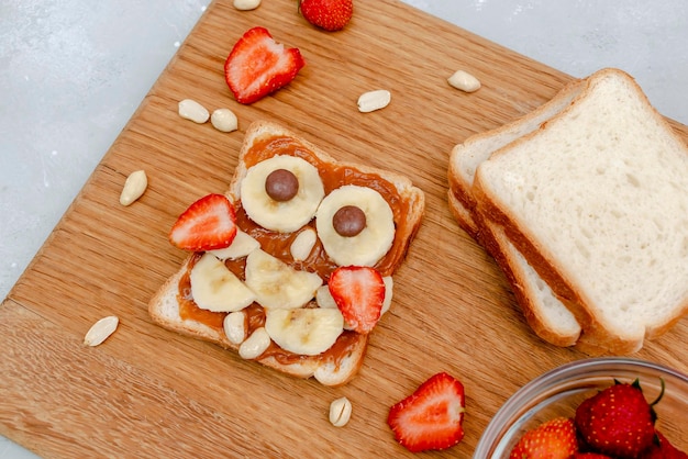 Funny hibou visage sandwich toast pain avec beurre de cacahuète banane fraise sur planche de bois mignon enfants enfants bébé dessert sucré petit déjeuner sain déjeuner art alimentaire sur fond gris vue de dessus