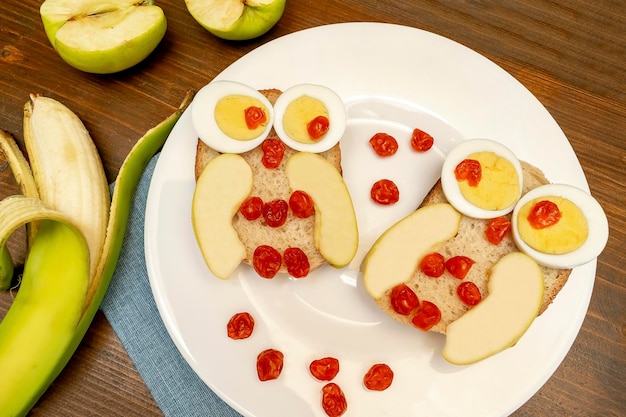 Funny hibou visage sandwich toast pain avec des œufs de poulet pomme banane fruits de baies séchées sur assiette enfants mignons dessert sucré petit déjeuner déjeuner art alimentaire sur fond en bois vue de dessus