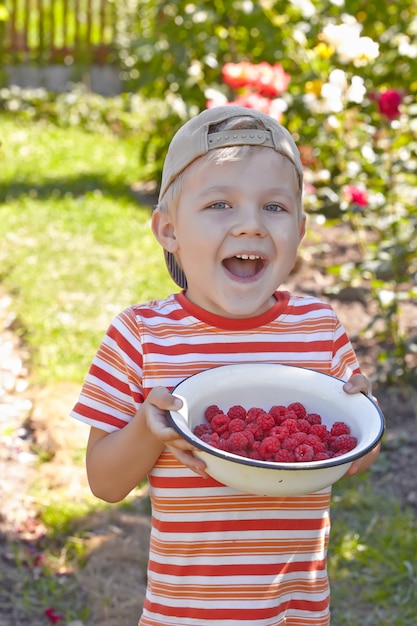 Funny kid boy avec bol d'une framboise mûre en plein air