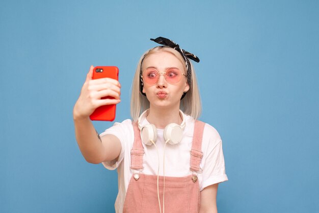 Funny teen girl fait selfie sur un smartphone, portant des vêtements lumineux et des lunettes de soleil roses