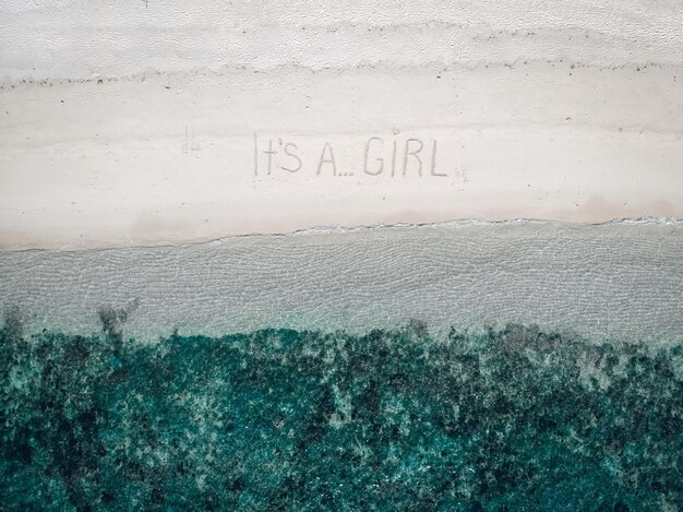 Le futur père inspiré a écrit une phrase "C'est une fille" sur le sable au bord des eaux turquoises, vue aérienne.