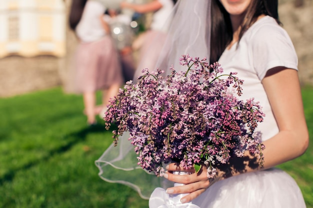 Future mariée tenant des fleurs lilas et une petite amie en arrière-plan, fête de poule