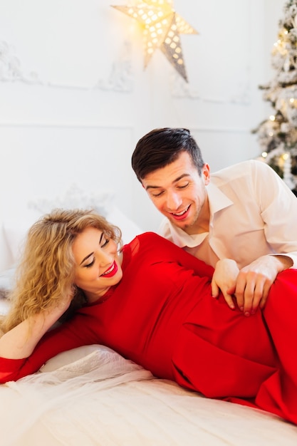 Les futurs parents attendent le bébé et sourient sur le lit à l'arbre de Noël