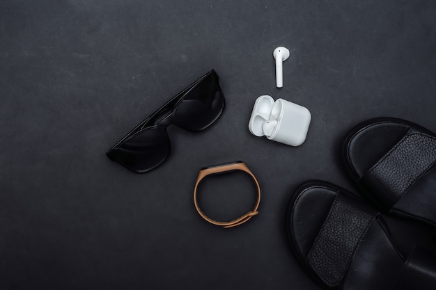 Gadgets et accessoires pour femmes sur fond noir. Sandales, bracelet intelligent, écouteurs sans fil, lunettes de soleil. Vue de dessus. Mise à plat