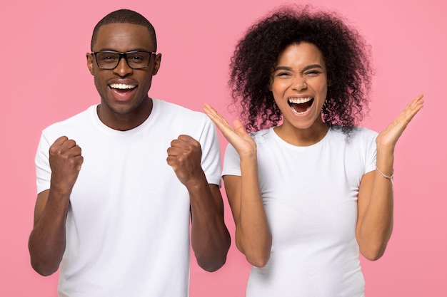 Photo les gagnants du couple de familles afro-américaines excitées et ravies célèbrent la victoire profitent de la victoire se réjouissent du succès heureux homme et femme noirs euphoriques extatiques criant de joie isolés sur fond de studio rose
