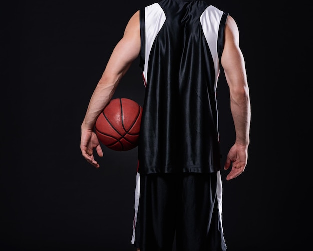 Les gagnants n'abandonnent jamais et les lâcheurs ne gagnent jamais Vue arrière courte d'un joueur de basket-ball tenant un ballon de basket sur fond noir